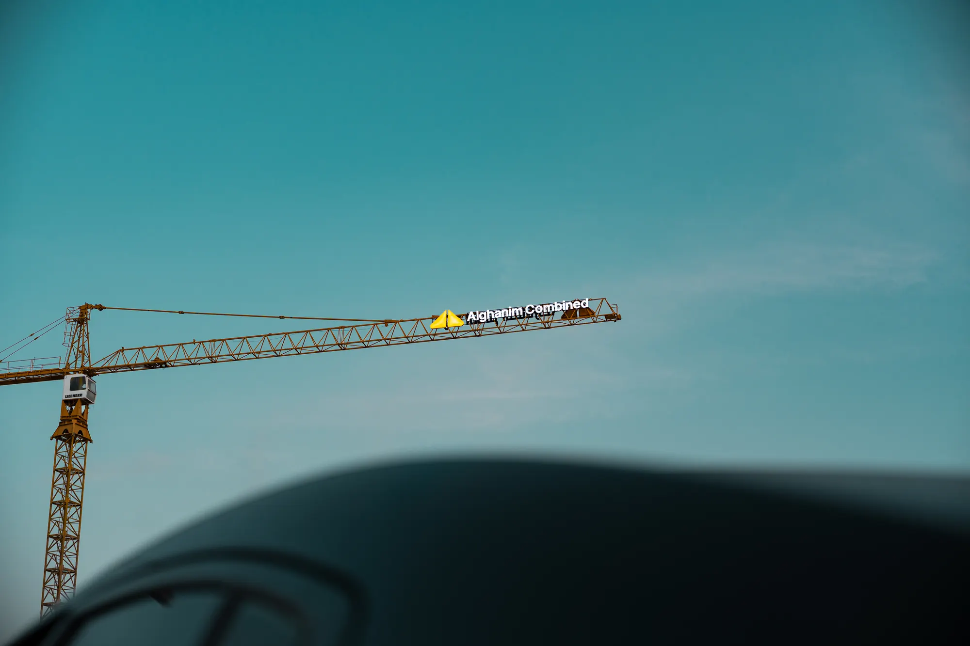 Alghanim Combined logo on the arm of a tower crane against a teal sky